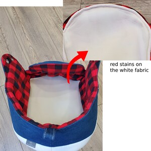 May include: A blue denim and white pet bed with a red and black plaid interior. The bed has a rounded shape with ear-like flaps. The interior has red stains on the white fabric.