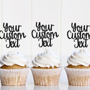 May include: Three cupcakes with white frosting in pleated paper liners, each topped with a black glittery cake topper featuring the text Your Custom Text in a cursive font. The toppers are mounted on thin white sticks inserted into the frosting.