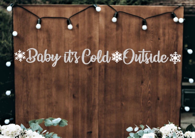May include: A silver glitter banner with the text "Baby it's Cold Outside" and snowflakes on a wooden background.