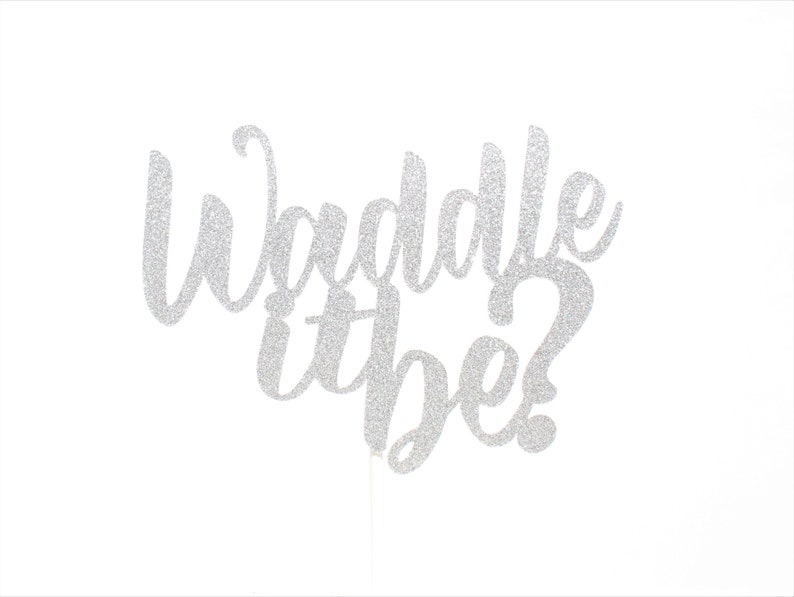 Pu&ograve; includere: Un topper per torta con glitter argento che presenta il testo in corsivo Waddle it be? con un punto interrogativo alla fine. Le lettere sono collegate in uno stile di scrittura fluido e hanno una finitura testurizzata e scintillante che riflette la luce.