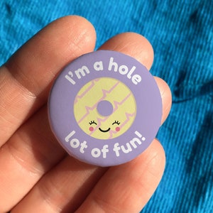 May include: Purple button with a yellow donut with a smiling face and the text "I'm a hole lot of fun!"