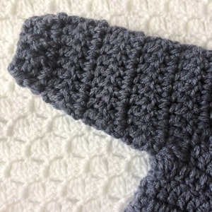 Puede incluir: Primer plano de una tela de crochet gris oscuro con un patr&oacute;n de puntadas texturizadas. La tela est&aacute; sobre un fondo de crochet blanco.