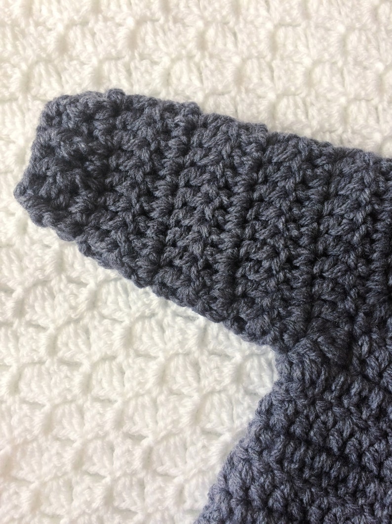 Puede incluir: Primer plano de una tela de crochet gris oscuro con un patr&oacute;n de puntadas texturizadas. La tela est&aacute; sobre un fondo de crochet blanco.