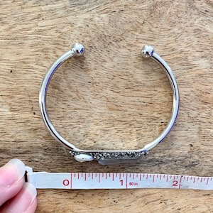 May include: A silver bangle bracelet with a small, rectangular piece of pyrite and a pearl attached to the front. The bracelet is 1 inch in diameter.