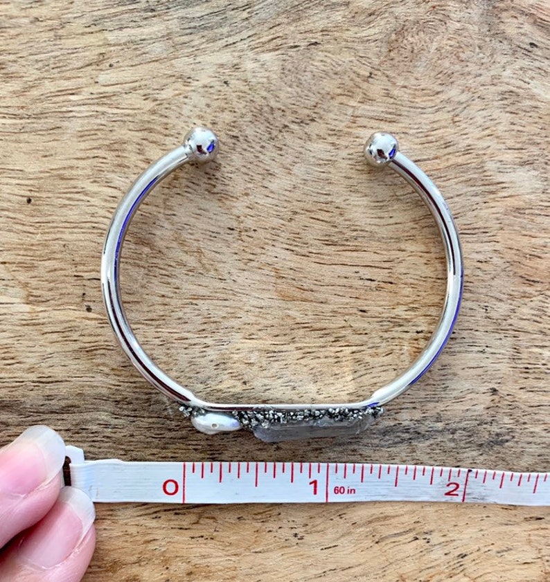 May include: A silver bangle bracelet with a small, rectangular piece of pyrite and a pearl attached to the front. The bracelet is 1 inch in diameter.