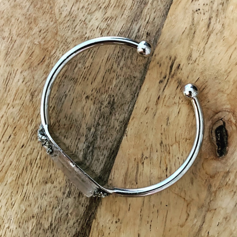 May include: Silver bangle bracelet with a clear crystal stone set in a silver frame. The bracelet has a simple design and is perfect for everyday wear.