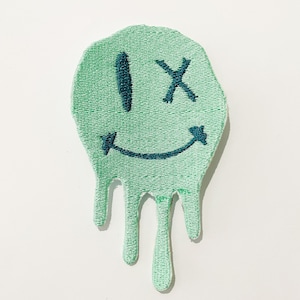 May include: Green embroidered patch with a dripping smiley face with an 'X' over one eye.