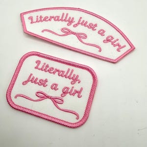 May include: Two embroidered patches with the phrase "Literally just a girl" in pink script. One patch is rectangular, the other is arched. Both have a white background and a pink bow design.