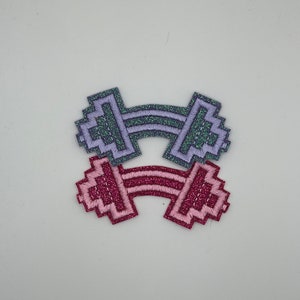 May include: Two glitter iron-on patches shaped like dumbbells. One is purple and the other is pink.