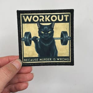 May include: Black and white patch with a black cat lifting a barbell. The text on the patch reads "WORKOUT BECAUSE MURDER IS WRONG".