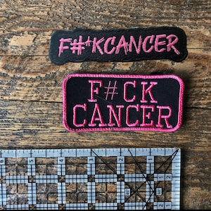 May include: Two black fabric patches with pink embroidered lettering. The top patch reads "F#KCANCER" and the bottom patch reads "F#CK CANCER".