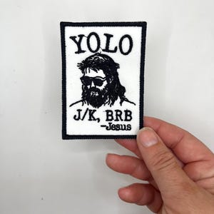 May include: Embroidered patch with a black border and a white background. The patch features a black and white image of a person with sunglasses and a beard. The text "YOLO" is above the image, and "J/K, BRB -Jesus" is below.