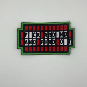 May include: An embroidered patch in green and red with the text "F*ck Around And Find Out" in black and white.