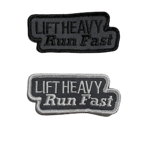 May include: Two black and gray embroidered patches with white stitching. The patches are rectangular with rounded corners. The text on the patches reads "Lift Heavy Run Fast".