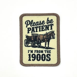May include: A rectangular patch with a tan background and a brown border. The patch features a horse-drawn carriage illustration and the text "Please be PATIENT I'M FROM THE 1900S" in black lettering.