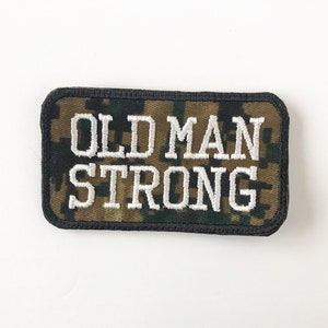 May include: A rectangular patch with a camouflage pattern and the text "OLD MAN STRONG" in white embroidery.