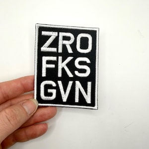 May include: Black and white embroidered patch with the text "ZRO FKS GVN" in a bold, sans-serif font. The patch is rectangular with a black background and white lettering, suitable for jackets, bags, or other fabric items.