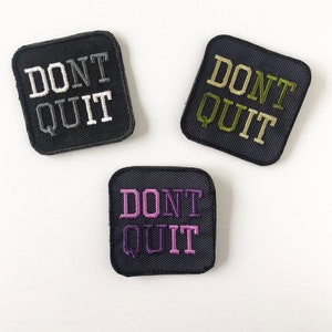 May include: Three black square patches with white, green, and purple embroidery that reads "DON'T QUIT".