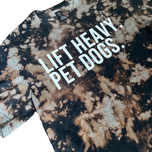 May include: A black and brown tie-dye t-shirt with the text "Lift Heavy. Pet Dogs." printed in white.