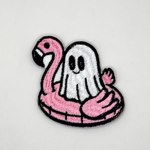 May include: Embroidered patch featuring a white ghost with a smiling face, floating on a pink flamingo pool float. The patch has a black border. The flamingo has a black beak and eye. The patch is on a white background.