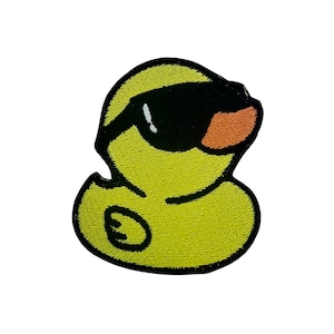 Peut inclure: Canard en caoutchouc jaune portant des lunettes de soleil noires. Le canard a un contour noir et un petit bec orange.
