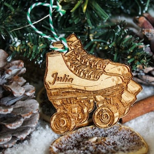 May include: A wooden Christmas bauble shaped like a pair of roller skates with the name "Julia" engraved on the side. The bauble is decorated with a green and white string.