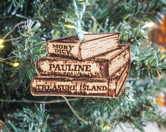 May include: Wooden Christmas ornament shaped like a stack of books. The books are labeled "Moby Dick", "Pauline", and "Treasure Island".