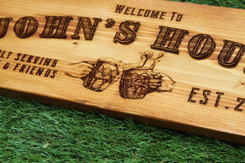 May include: Wooden sign with the text "Welcome to John's House" and "Est. 2" with a graphic of two hands holding beer mugs and a beer foam splash.
