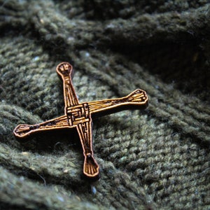 May include: A wooden Celtic cross pin with intricate details, resting on a green knitted fabric.