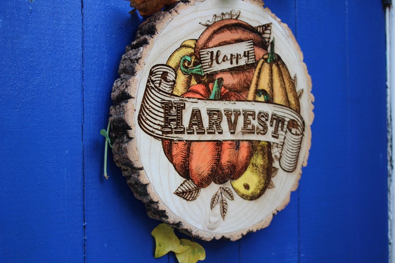 May include: A wooden round sign with a rustic bark edge, featuring a hand-drawn illustration of pumpkins, gourds, and leaves. The sign has the text "Happy Harvest" in a banner.