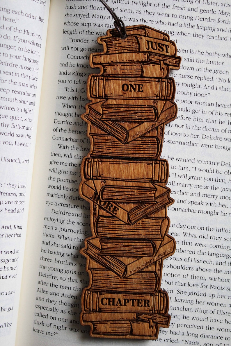 May include: A wooden bookmark with a stack of books design. The bookmark has the words "Just One More Chapter" on it.