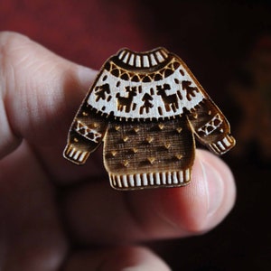 May include: A wooden Christmas ornament shaped like a brown sweater with white trim and a reindeer pattern.