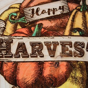 May include: A wood slice with a burnt-in design of pumpkins and a banner that reads "Happy Harvest".