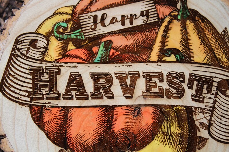 May include: A wood slice with a burnt-in design of pumpkins and a banner that reads "Happy Harvest".