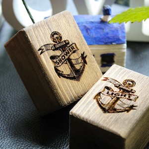 Pode incluir: Dois blocos de madeira com uma âncora e as palavras "Chuveiro" e "Luz" gravadas neles. Os blocos são manchados de uma cor marrom escura.