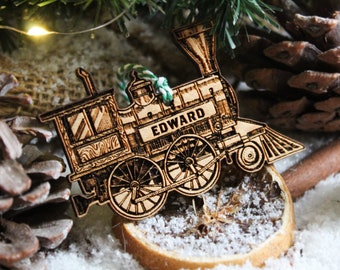 May include: Wooden Christmas ornament shaped like a vintage train engine with the name "EDWARD" printed on the side. The ornament is brown and has a green string attached to it.