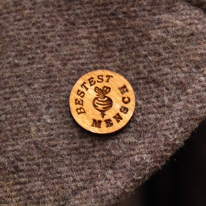 Op de afbeelding: Een houten knoop met de tekst "BESTES MENSC" en een kleine biet-illustratie in het midden.