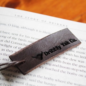 May include: A brown leather bookmark with the text "Dibbly Yak Co." in black lettering. The bookmark is lying on a book with text about the story of Deirdre.