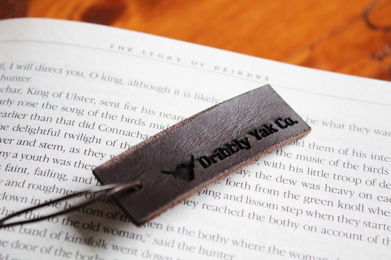 May include: A brown leather bookmark with the text "Dibbly Yak Co." in black lettering. The bookmark is lying on a book with text about the story of Deirdre.