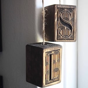 May include: Two wooden blocks with the letters "I" and "S" carved into them. The blocks are hanging from a string and have a dark wood stain.