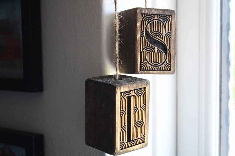 May include: Two wooden blocks with the letters "I" and "S" carved into them. The blocks are hanging from a string and have a dark wood stain.