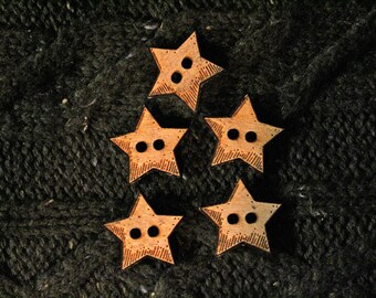 May include: Five wooden star-shaped buttons with two holes each. The buttons are a light brown colour and have a slightly textured surface. They are arranged in a pyramid shape on a dark green knitted fabric.