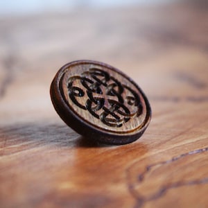 Op de afbeelding: Een houten knoop met een gesneden Keltisch knoopontwerp. De knoop is bruin en heeft een gladde, gepolijste afwerking.