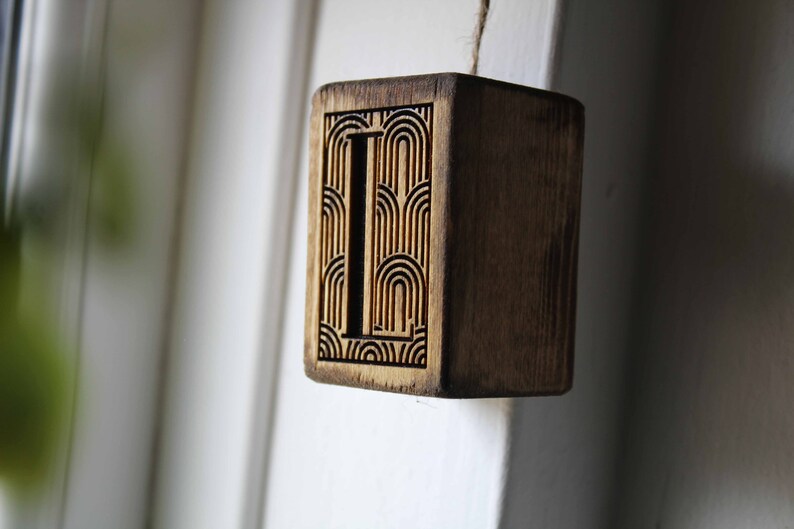 May include: A wooden block with the letter "L" carved into it. The letter is surrounded by a geometric pattern.