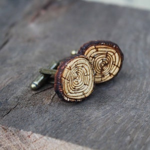 Peut inclure: Une paire de boutons de manchette en bois avec un motif de cernes d'arbre. Les boutons de manchette sont bruns et ont une couleur de bois clair au centre.