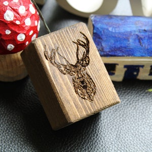 Può includere: Un blocco di legno con un disegno di testa di cervo bruciato sulla superficie. Il blocco è marrone scuro e ha un aspetto rustico.