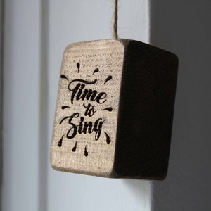 May include: A wooden sign with the text "Time to Sing" in a decorative font. The sign is hanging from a string and has a rustic, natural look.