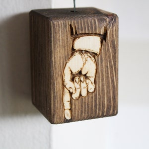 Pode incluir: Um bloco de madeira com uma mão apontando para baixo, queimado na superfície. O bloco é marrom escuro com um padrão de grão de madeira.