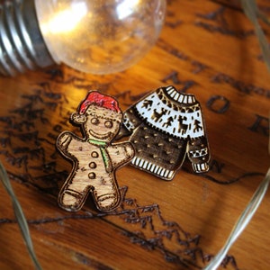 May include: Two wooden Christmas ornaments, a gingerbread person wearing a Santa hat and a brown and white patterned sweater.