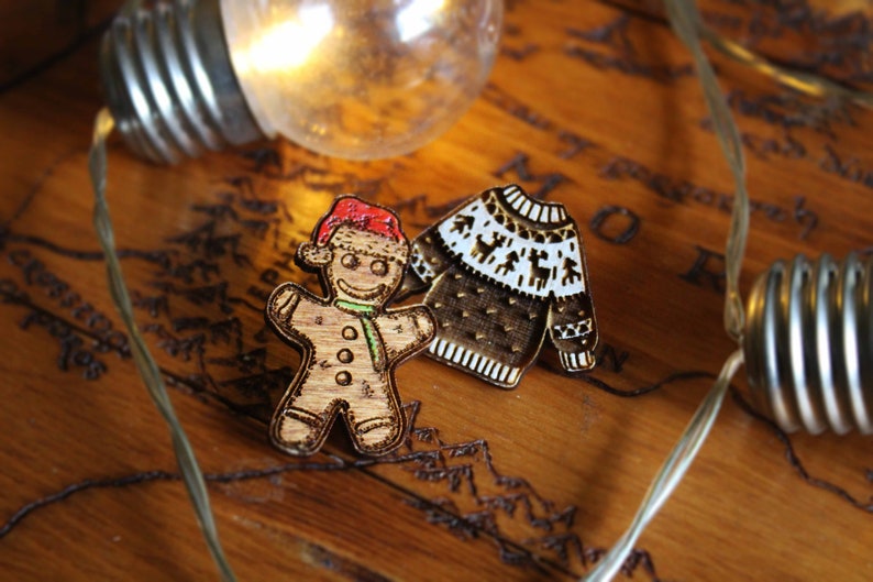 May include: Two wooden Christmas ornaments, a gingerbread person wearing a Santa hat and a brown and white patterned sweater.